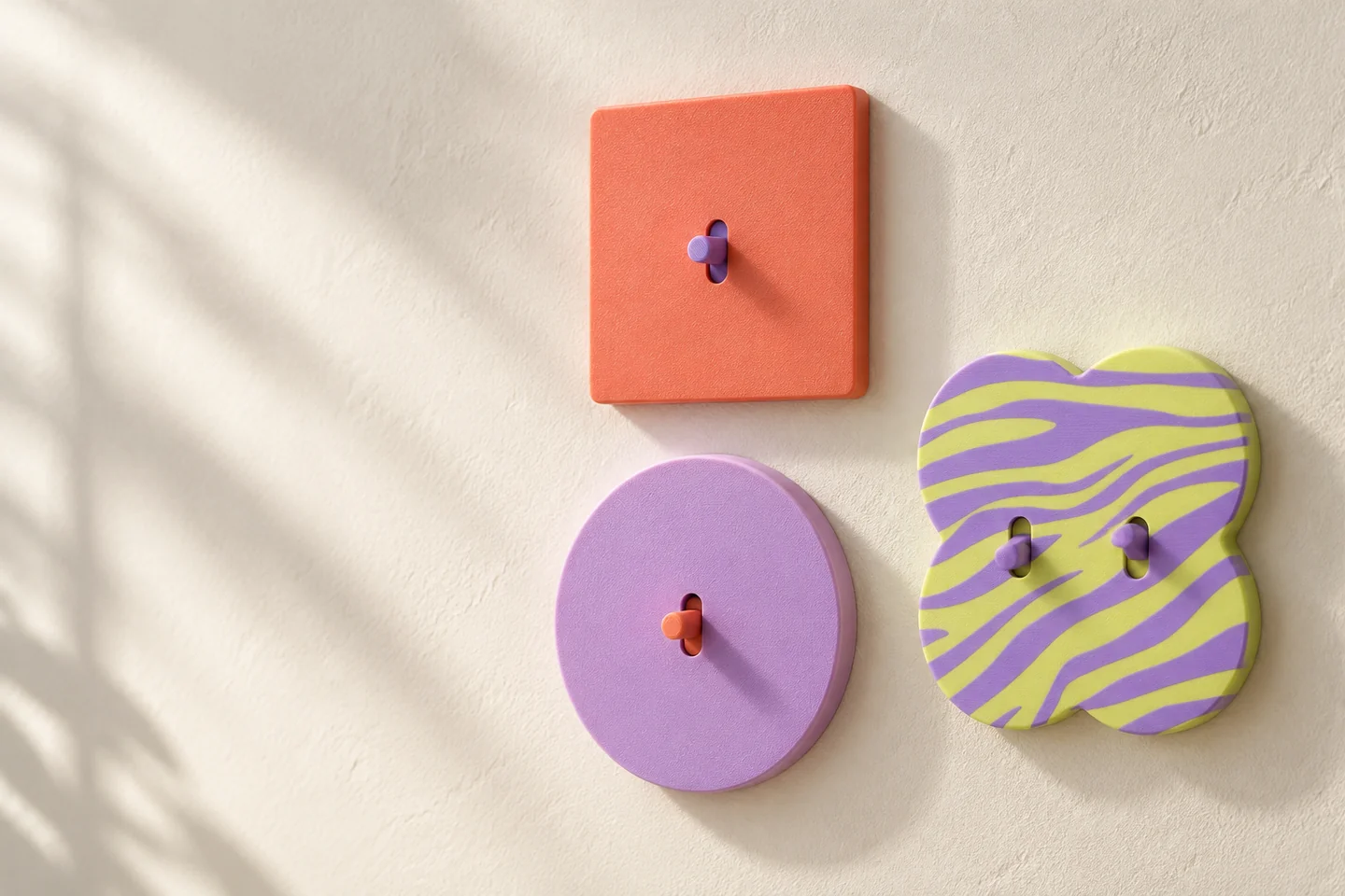 Three opaque switch covers on a wall: a coral square, a lilac circle and a wavy panel with two tabs
